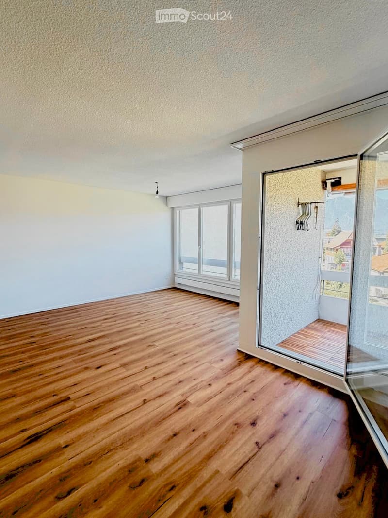Empty room with wooden flooring, large windows, and a sliding glass door leading to a balcony.