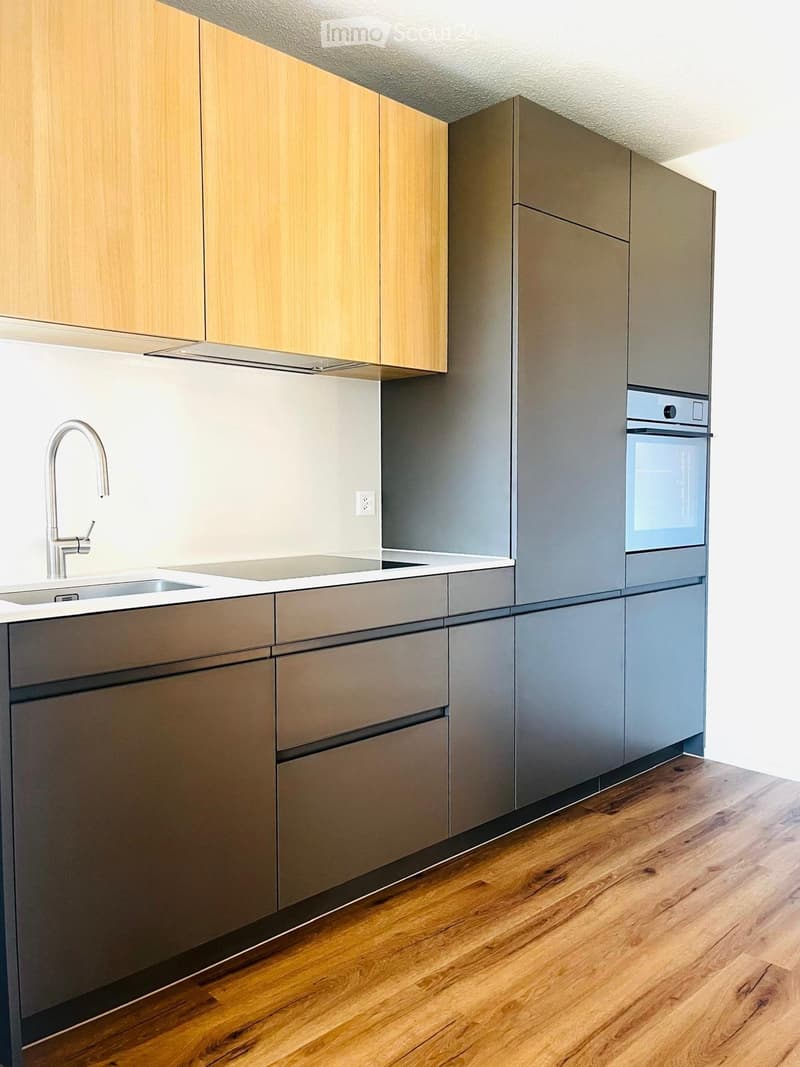 Modern kitchen with light wood and grey cabinets, stainless steel sink and faucet, and built-in oven.