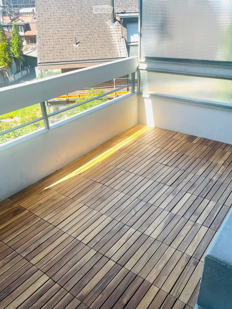 Balcony with wooden decking, white railing, and large windows overlooking a residential area.