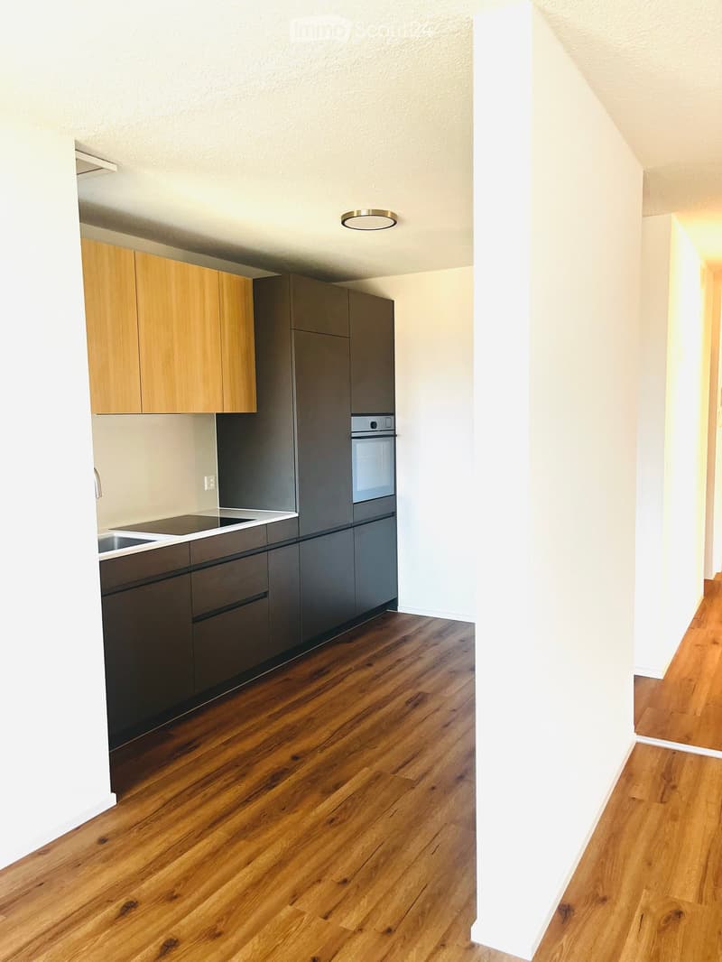 Modern kitchen with wooden and grey cabinets, stainless steel appliances, and a wooden floor.