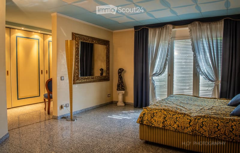 large bed, large mirror, decorative statues, wooden chair, tiled floor, window with blinds and curtains, power outlet