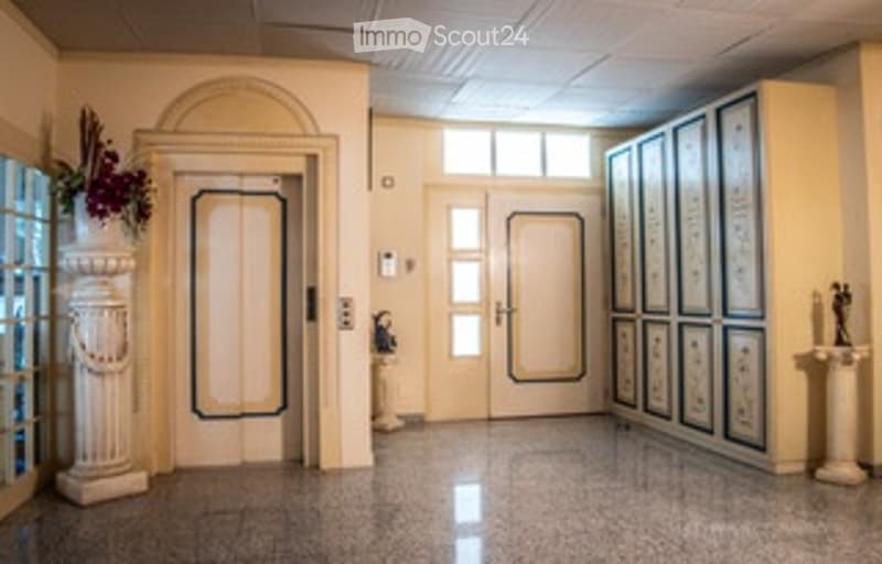 Grand hallway with polished marble floors, large double doors, decorative columns, and framed artwork on the walls.