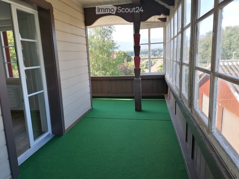 Balcony with green artificial turf flooring, large windows offering scenic views of trees and distant landscape.