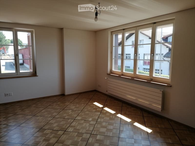 Empty room with wooden flooring, large windows, radiator, and natural light. No furniture or equipment present.