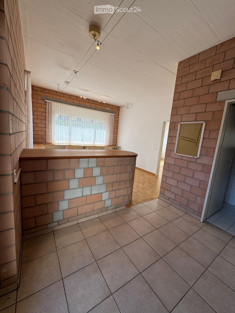 Empty room with tiled floor, brick walls, and a wooden counter. No furniture or equipment present.
