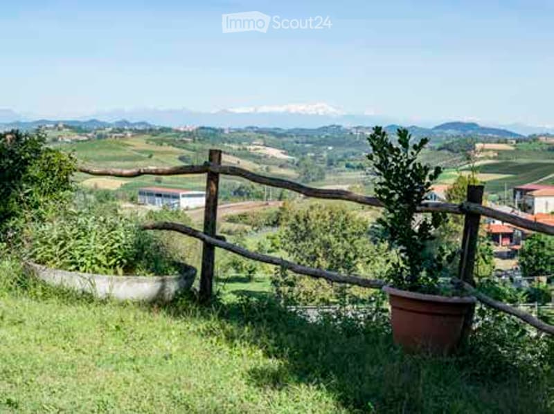 A serene outdoor garden area with a wooden fence, lush greenery, and a scenic mountain view in the background.