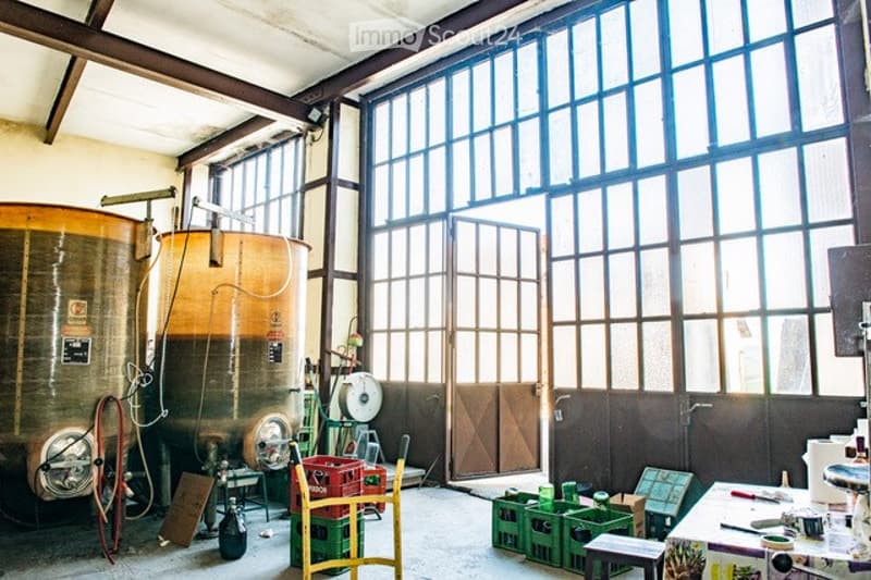 Industrial-style room with large windows, wooden beams, and metal casks. Contains a wooden chair, small table, crates, and various tools.