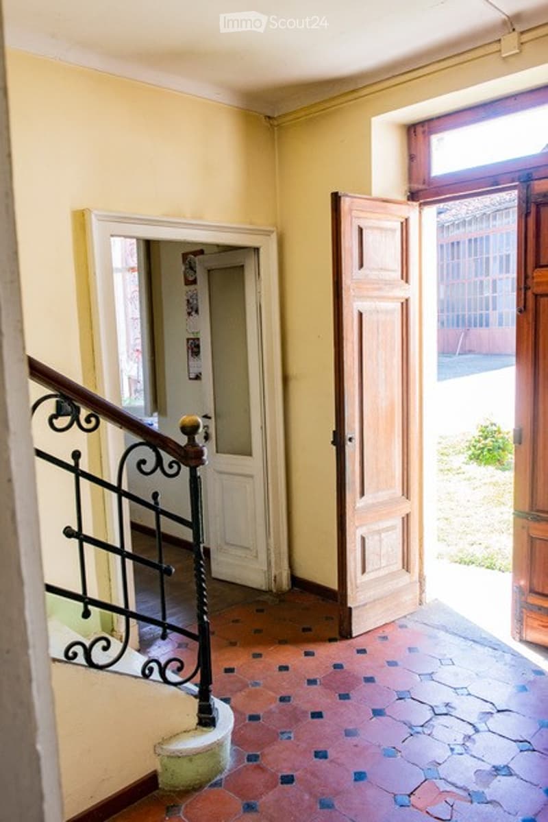 Hallway with a staircase leading upwards, featuring a black wrought iron railing, a wooden door, and a tiled floor.