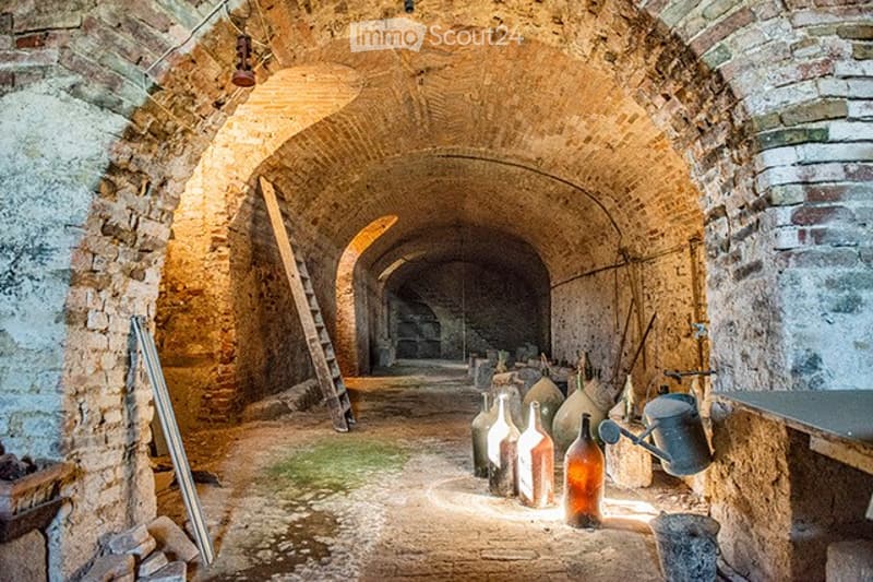 An old, rustic stone corridor with arched ceilings, wooden ladder, and scattered glass bottles and tools.