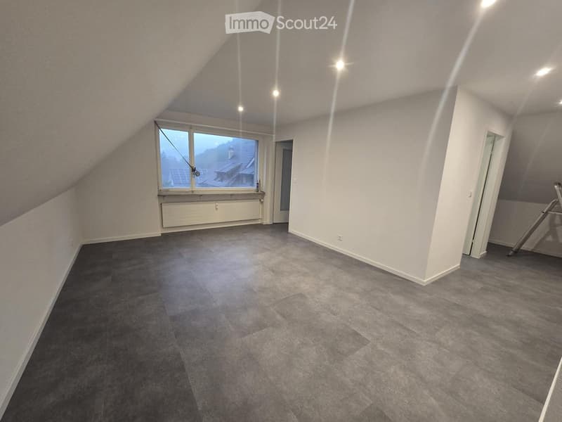 Empty attic room with grey carpeted floor, white walls, large window with view, and recessed lighting.