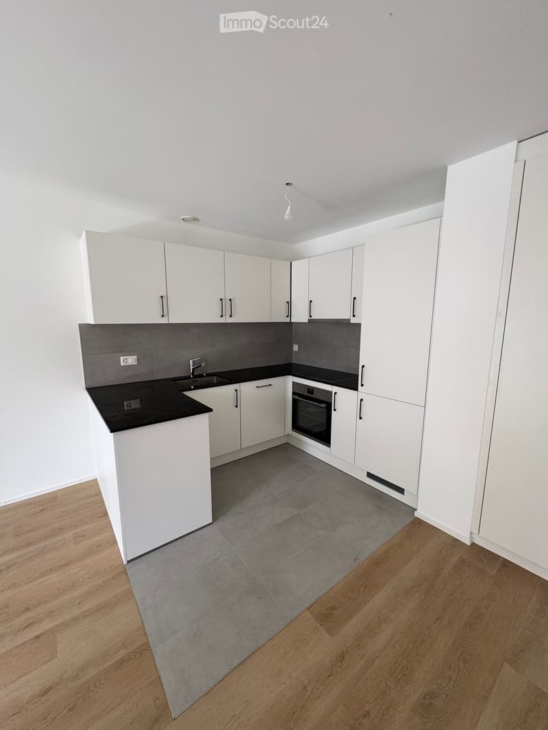 Modern kitchen with white cabinets, black countertops, and grey tiled backsplash. Features a sink, oven, and ample storage space.