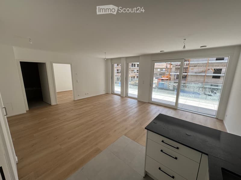Open-plan living and dining area with wooden flooring, large glass sliding doors leading to a balcony, and a modern kitchen island with drawers.