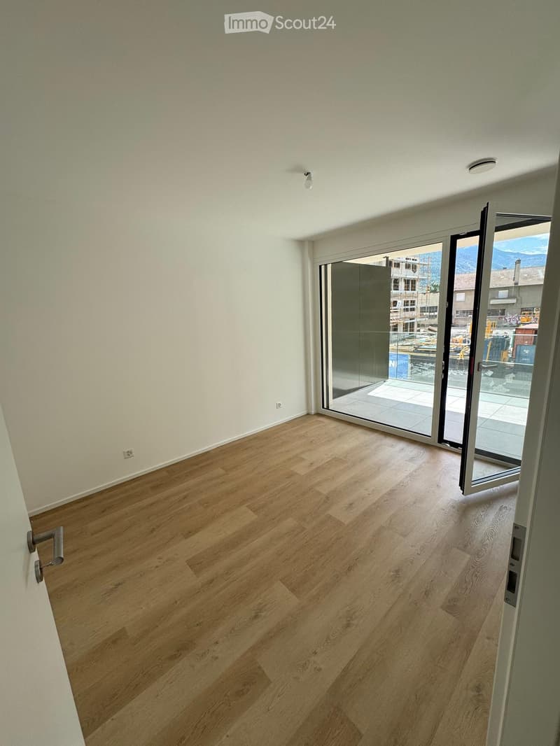 Empty room with light wooden flooring, white walls, and large glass sliding doors leading to a balcony.