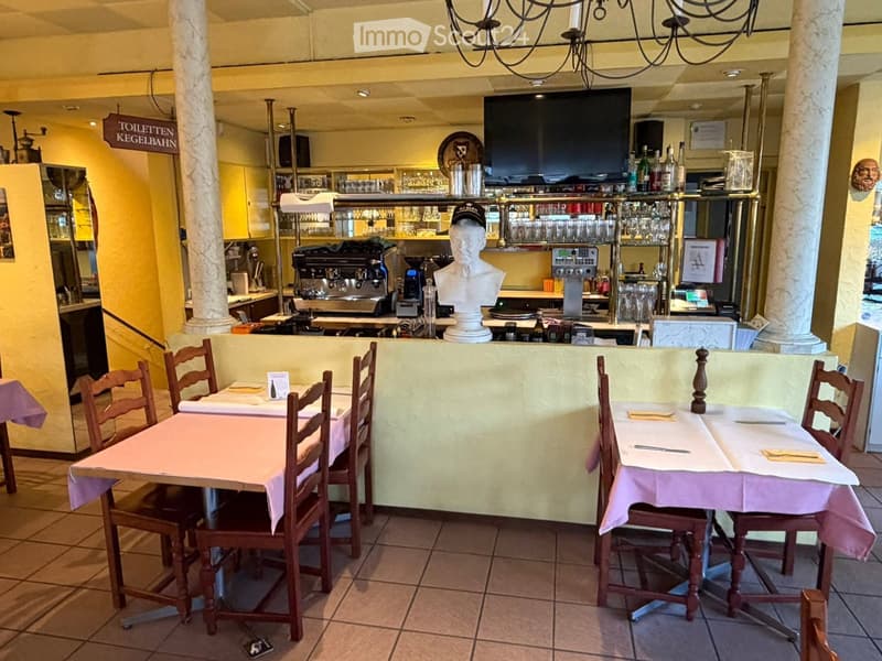 A restaurant interior with tables and chairs, a television, a refrigerator, a coffee machine, and a statue in the center.