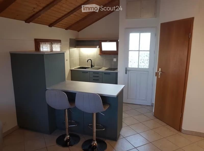 Modern kitchen with a grey cabinet island, two white stools, a sink with a faucet, and built-in cabinets.