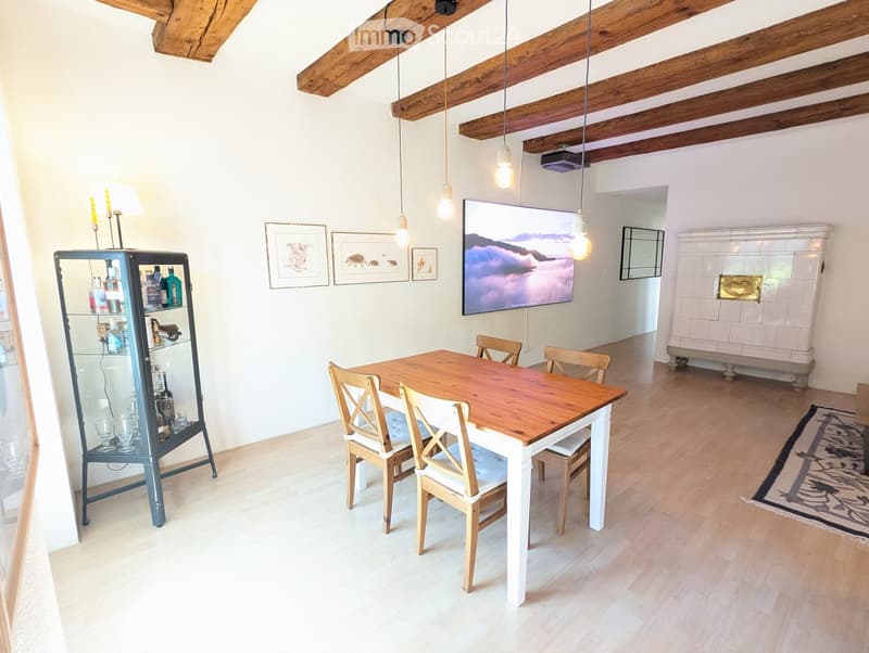 Dining room with wooden table, chairs, glass cabinet, TV screen, and artwork on the wall.