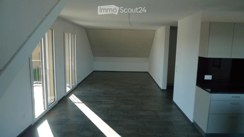 Empty room with slanted ceiling, dark tiled floor, large windows, and built-in cabinets.