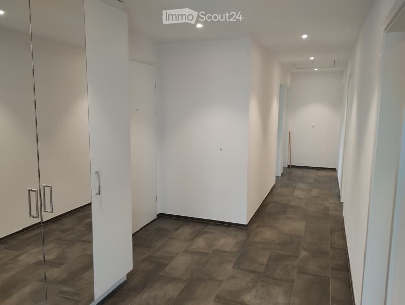A clean, modern hallway with dark tiled flooring and white walls. Features include a glass-paneled door on the left and a closed white door ahead.