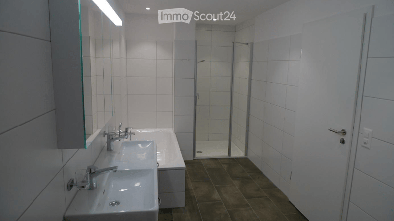 Modern bathroom with white tiles, two sinks, a bathtub, and a glass-enclosed shower area.