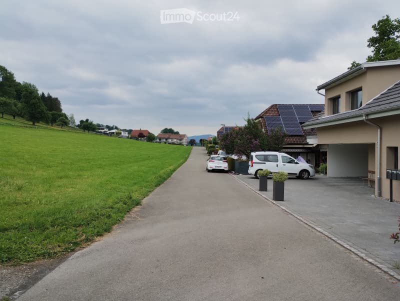 Residential street with houses, parked cars, and a garage visible on the right side.