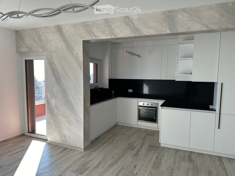 Modern kitchen with white cabinets, a built-in oven, and a sleek black countertop. Features a large sliding glass door leading to a balcony.