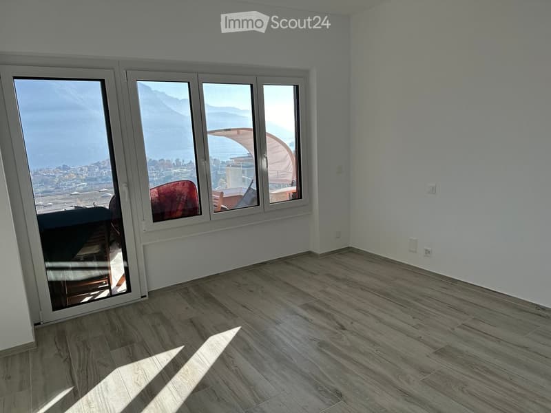 Empty room with light wooden flooring, large windows offering a scenic view, and white walls.