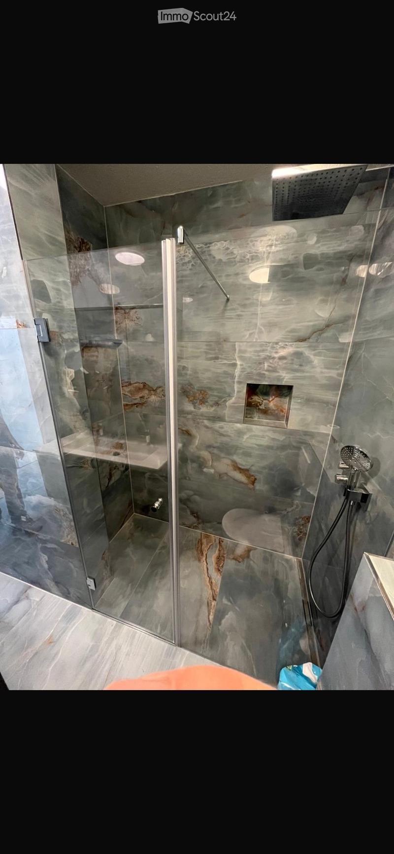 Modern bathroom with a large, sleek shower stall featuring a glass door, marble-like tiles, and a modern showerhead.