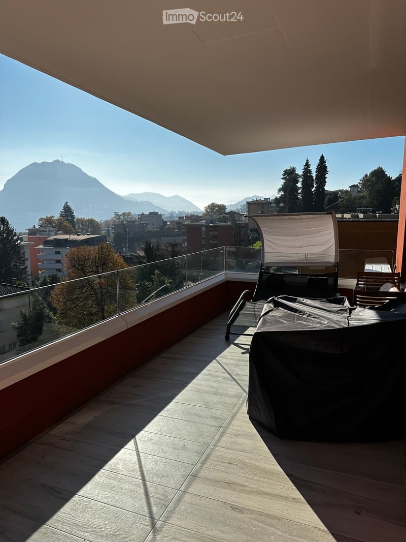 Balcony with wooden flooring, glass railing, covered seating area, and scenic mountain view.
