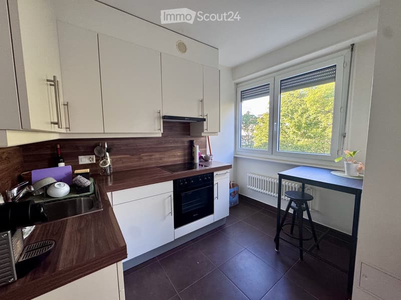 Modern kitchen with white cabinets, dark wooden countertops, and stainless steel appliances. Features a sink, oven, and a small dining area with a table and stool.