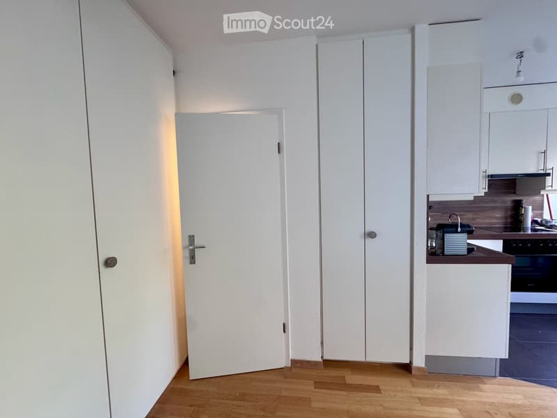 Modern kitchen with white cabinets, wooden floor, and a small coffee maker on the counter.