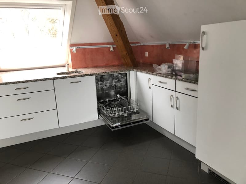 Modern kitchen with white cabinets, granite countertop, sink, and open dishwasher. Features a window with natural light and a slanted wooden ceiling beam.