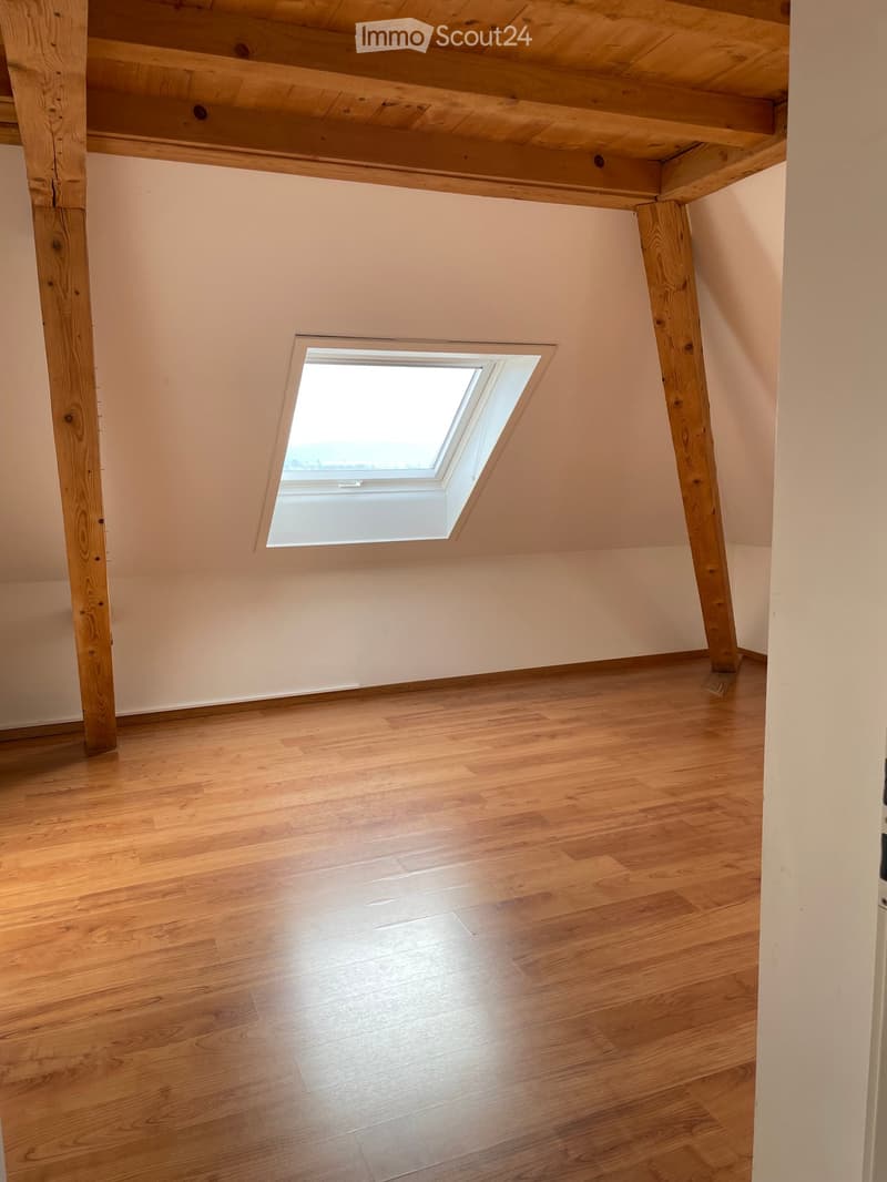 Empty attic room with wooden floor, exposed wooden beams, and a skylight window letting in natural light.