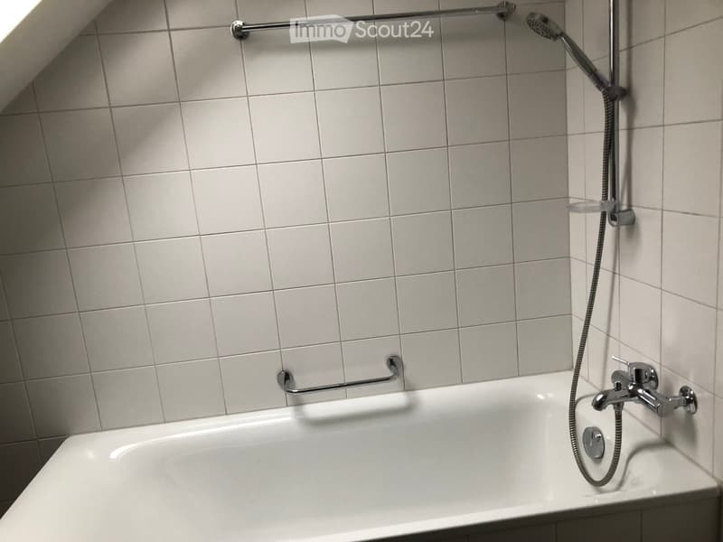 Bathtub with a modern chrome faucet and handheld showerhead, mounted on tiled walls with a grab bar for safety.