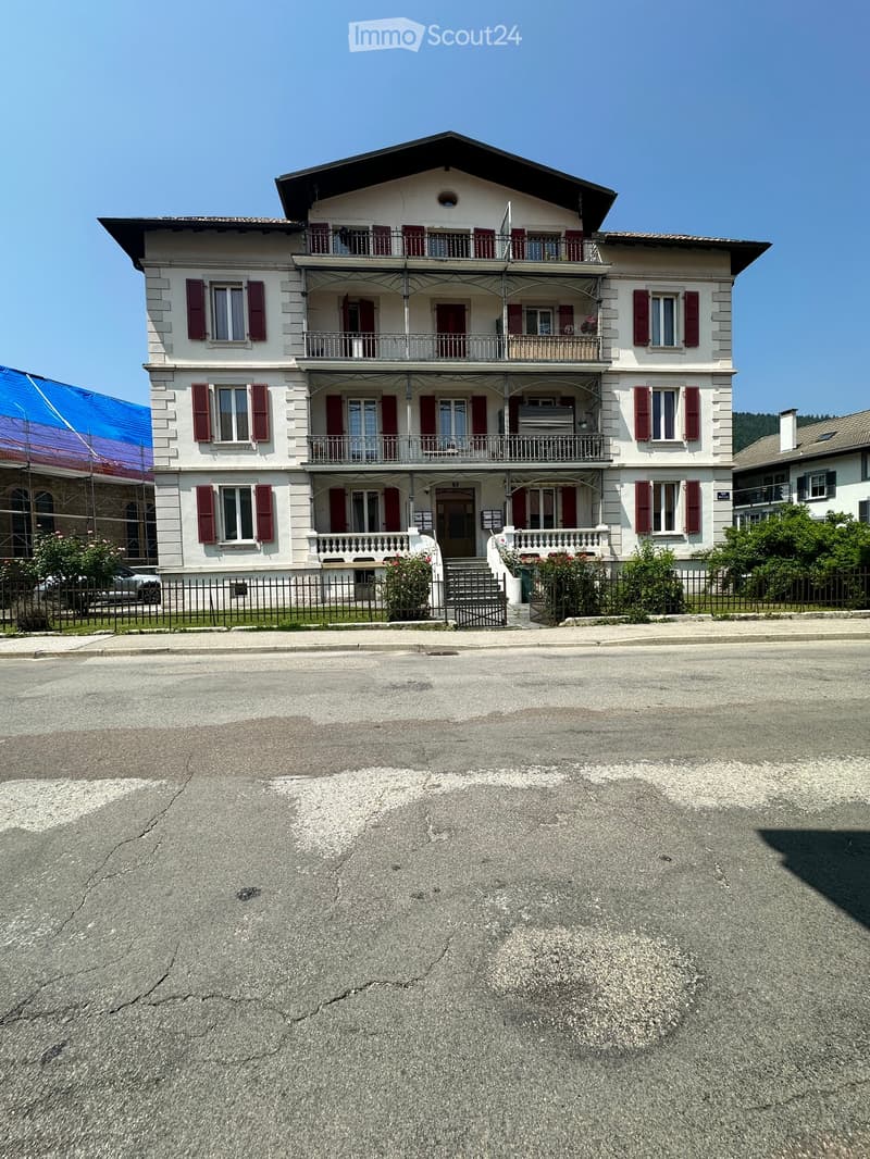 A three-story residential house with white walls, red shutters, multiple balconies, and a fenced front yard.
