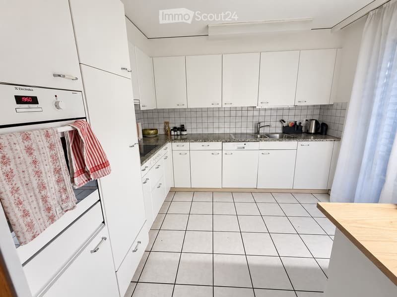 Modern kitchen with white cabinets, tiled floor, granite countertop, stainless steel sink, and wooden table.