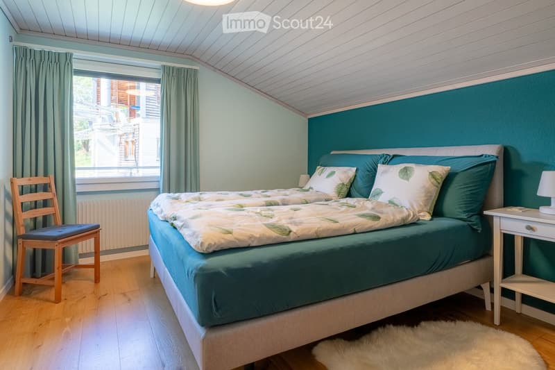 Cozy bedroom with a double bed, green bedding, a wooden chair, a nightstand, and a fur rug on the floor.