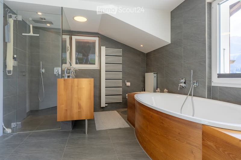 Modern bathroom with a wooden bathtub, glass-enclosed shower, wooden sink cabinet, radiator, and large window offering a scenic view.