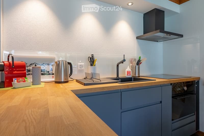 Modern kitchen with wooden countertops, stainless steel appliances, and grey cabinets. Features a sink, oven, and various kitchen utensils.
