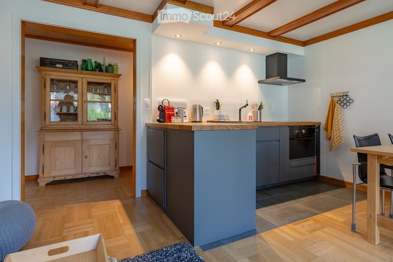 Modern kitchen with wooden beams, island, built-in appliances, and a wooden dining table with chairs.