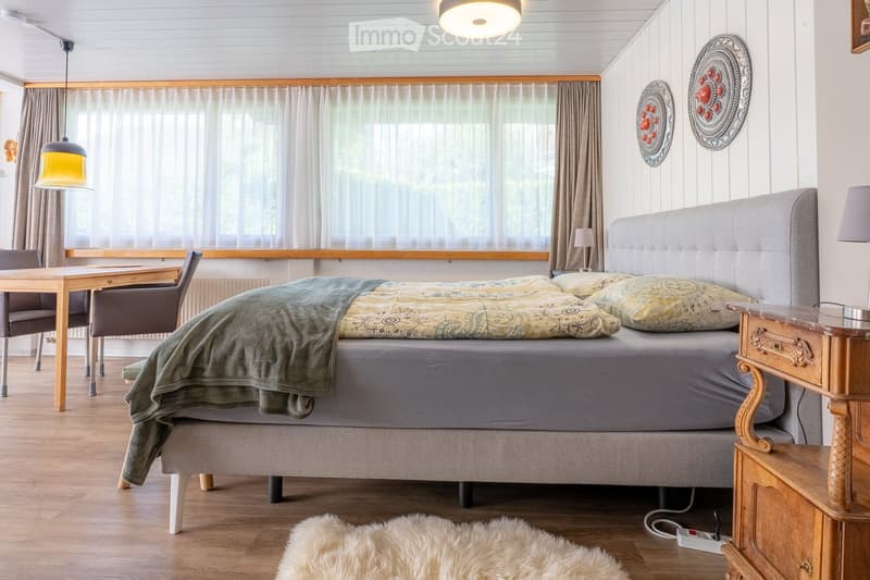 Cozy bedroom with a large bed, patterned bedding, nightstand, wooden table, and hanging pendant lights.