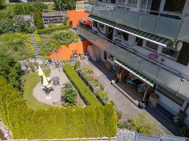 A multi-level garden area with a patio, seating, greenery, and a small lawn.