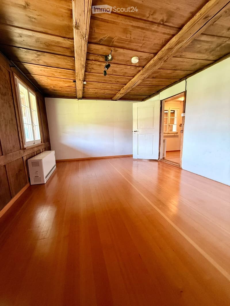 Empty room with wooden floor, white walls, wooden ceiling beams, and a white door leading to another room.