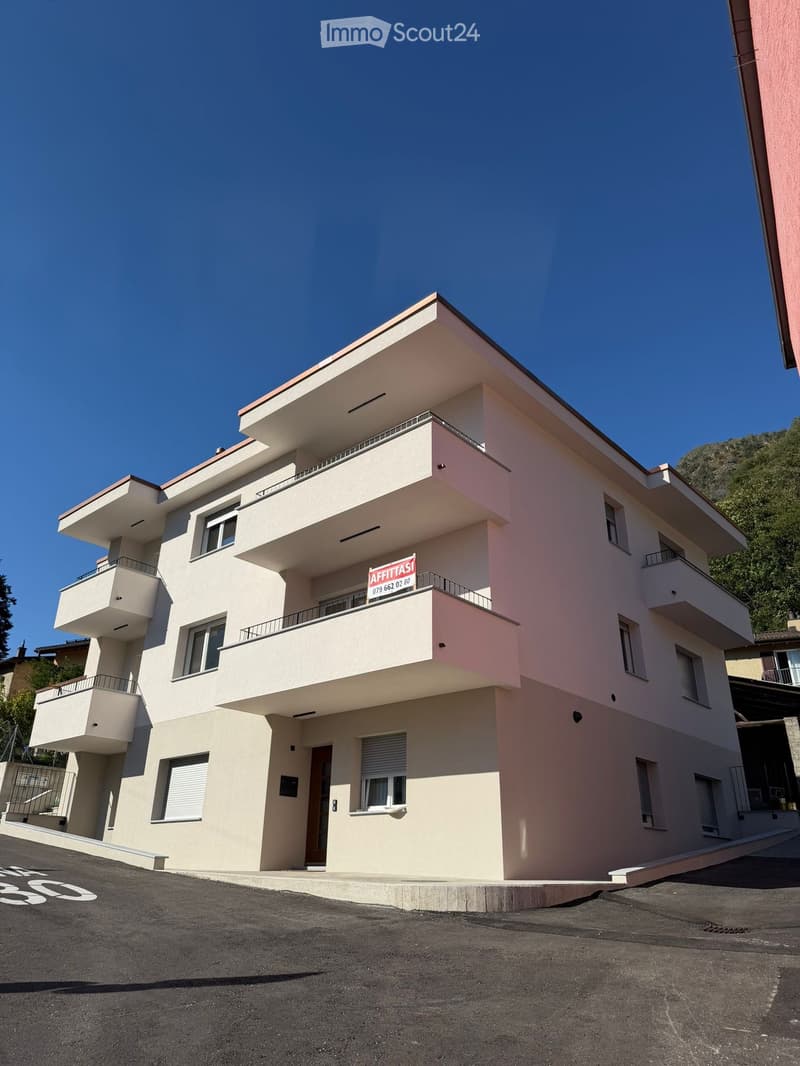 Modern two-story building with light pink facade, multiple balconies, and a sign reading "AFFITTASI" indicating rental availability.