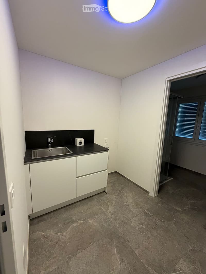Empty kitchen with white cabinets, a stainless steel sink, and a dark countertop. The floor is made of polished stone tiles, and there is a circular skylight above.