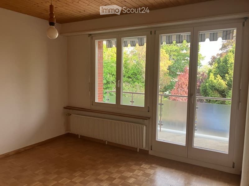 Empty room with wooden flooring, large windows, radiator, and access to a balcony.