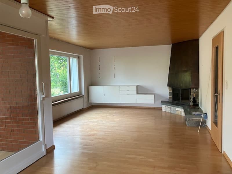Bright, unfurnished room with wooden flooring, white cabinetry, large windows, and a fireplace area.