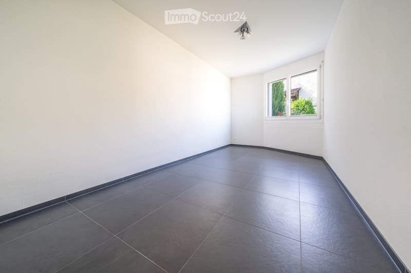 Empty room with white walls, dark tiled floor, and a single window with white frame. No furniture or equipment present.