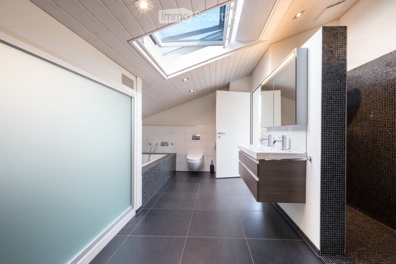 Modern bathroom with dark tiled floor, white walls, a bathtub, toilet, sink with faucet, and a mirrored cabinet. Features a skylight window and sleek design.