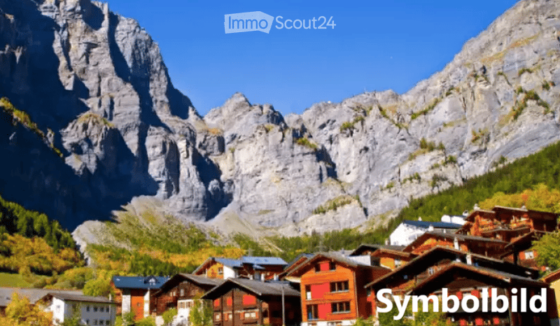 Village with traditional wooden houses nestled in a valley surrounded by towering mountains under a clear blue sky.