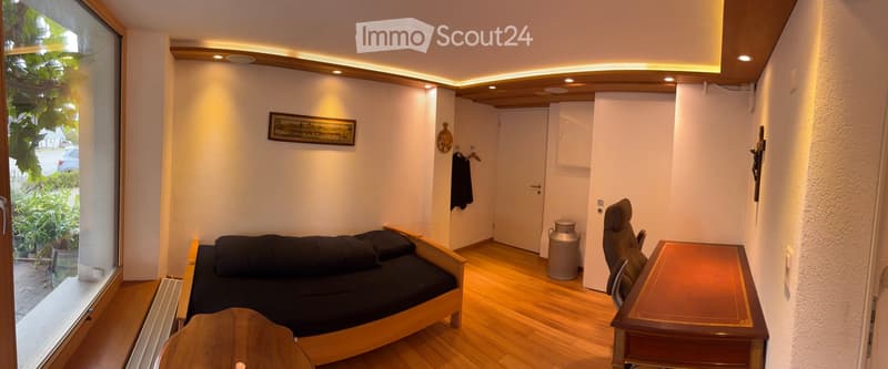 Cozy, compact room with wooden flooring, a small sofa, a table, a chair, a picture frame on the wall, and a small cabinet.